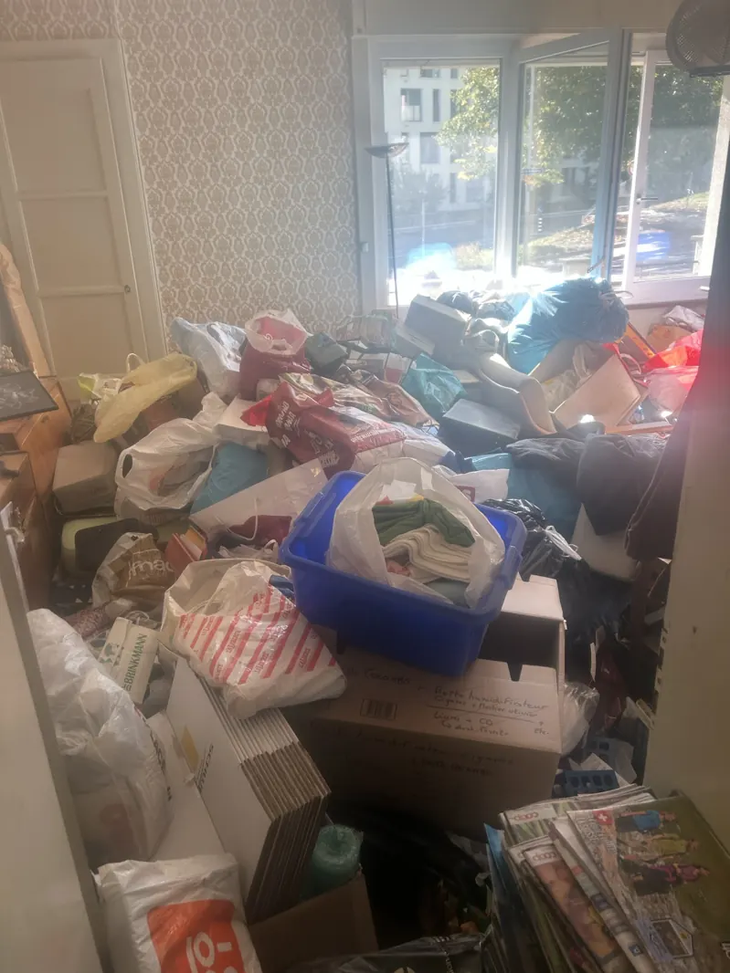 Pièce d'appartement remplie de sacs, cartons et magazines avant un débarras complet à Fribourg