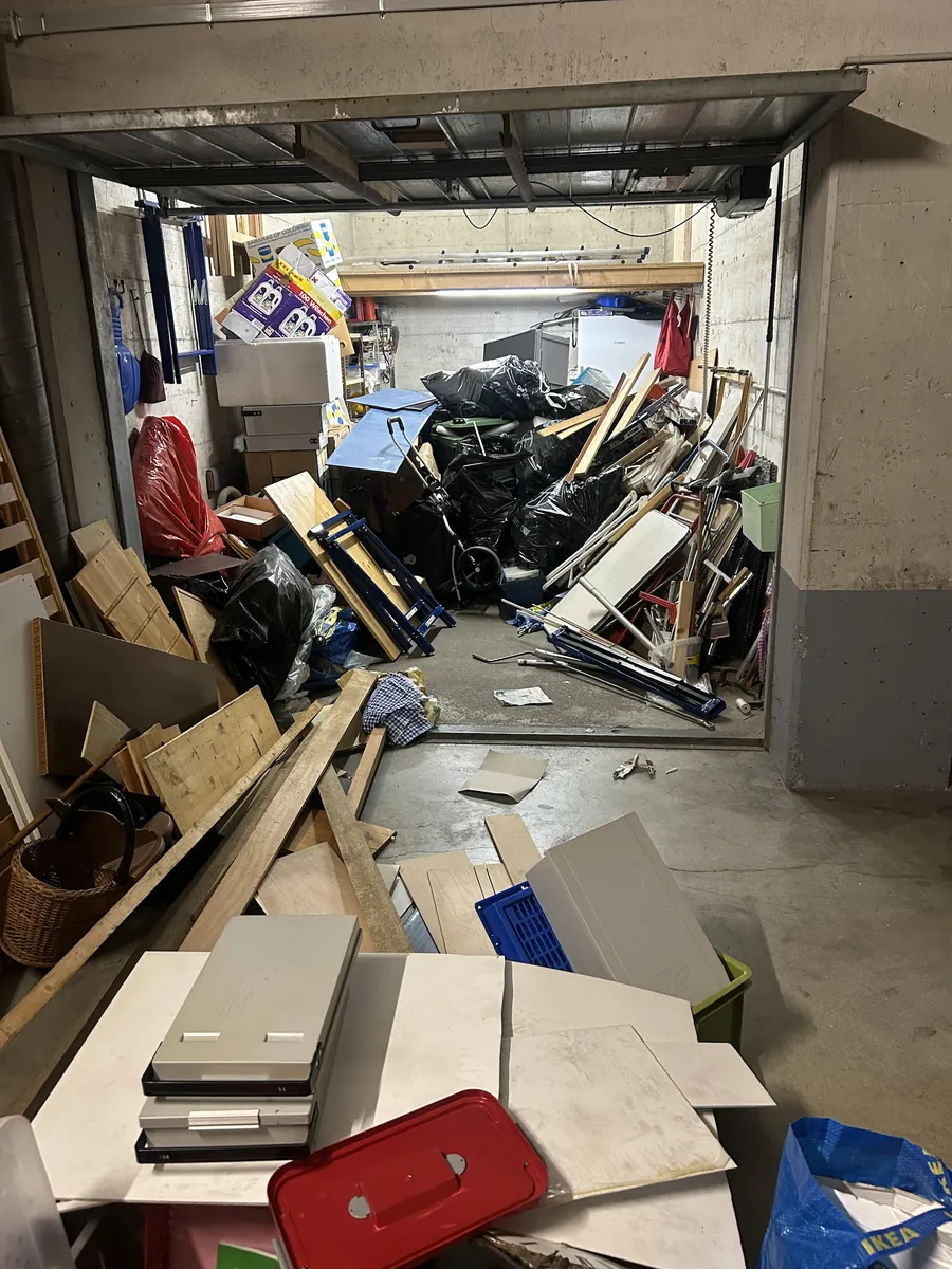 Garage encombré avant débarras à Fribourg : meubles démontés, planches, sacs et encombrants empilés du sol au plafond