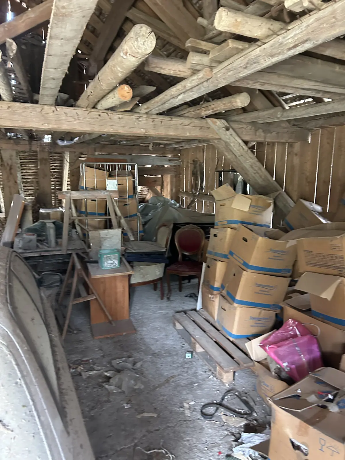 Grenier de grange sous charpente rempli de cartons et vieux meubles avant débarras, région de Fribourg
